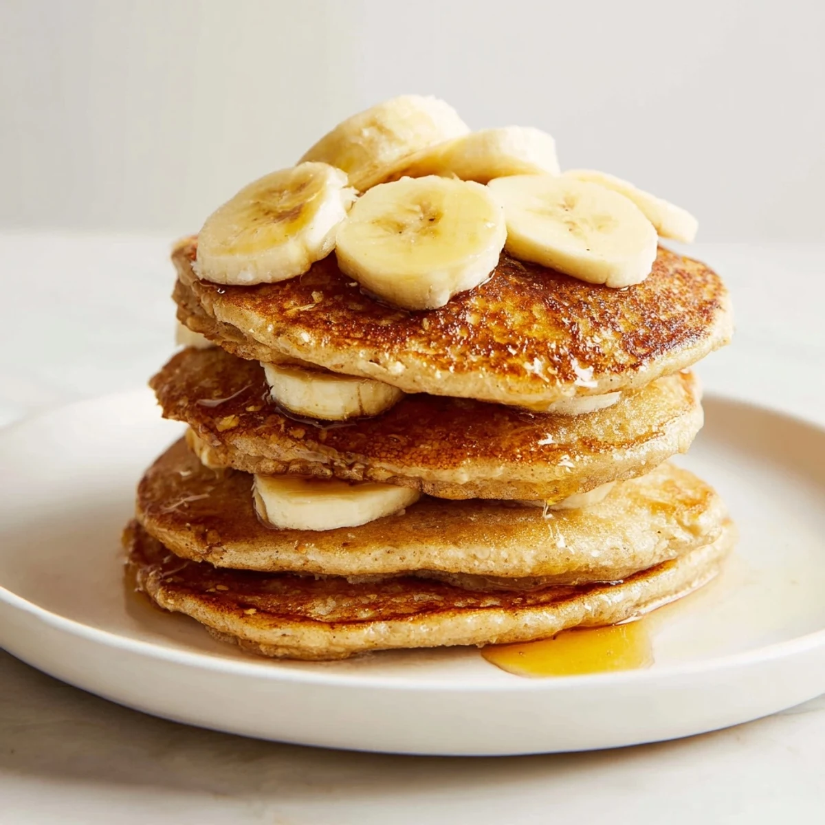 Golden banana oat pancakes stacked high, drizzled with sweet maple syrup for breakfast.