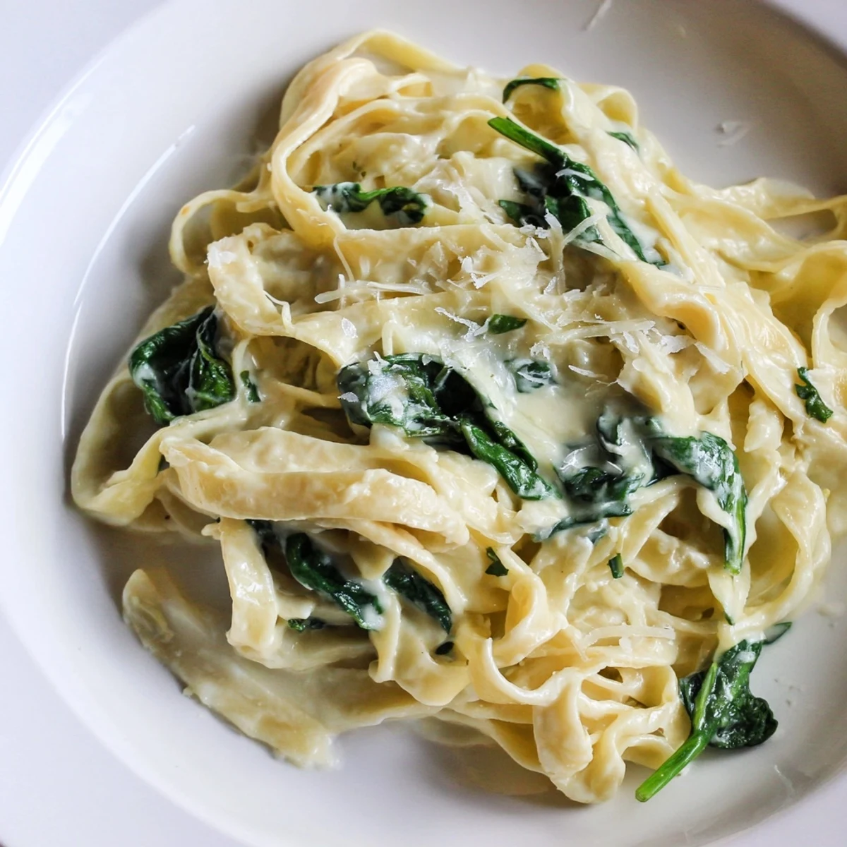 A close-up of Creamy Garlic Spinach Pasta, garnished with fresh parsley and grated Parmesan, steam rising from the rich, velvety sauce.