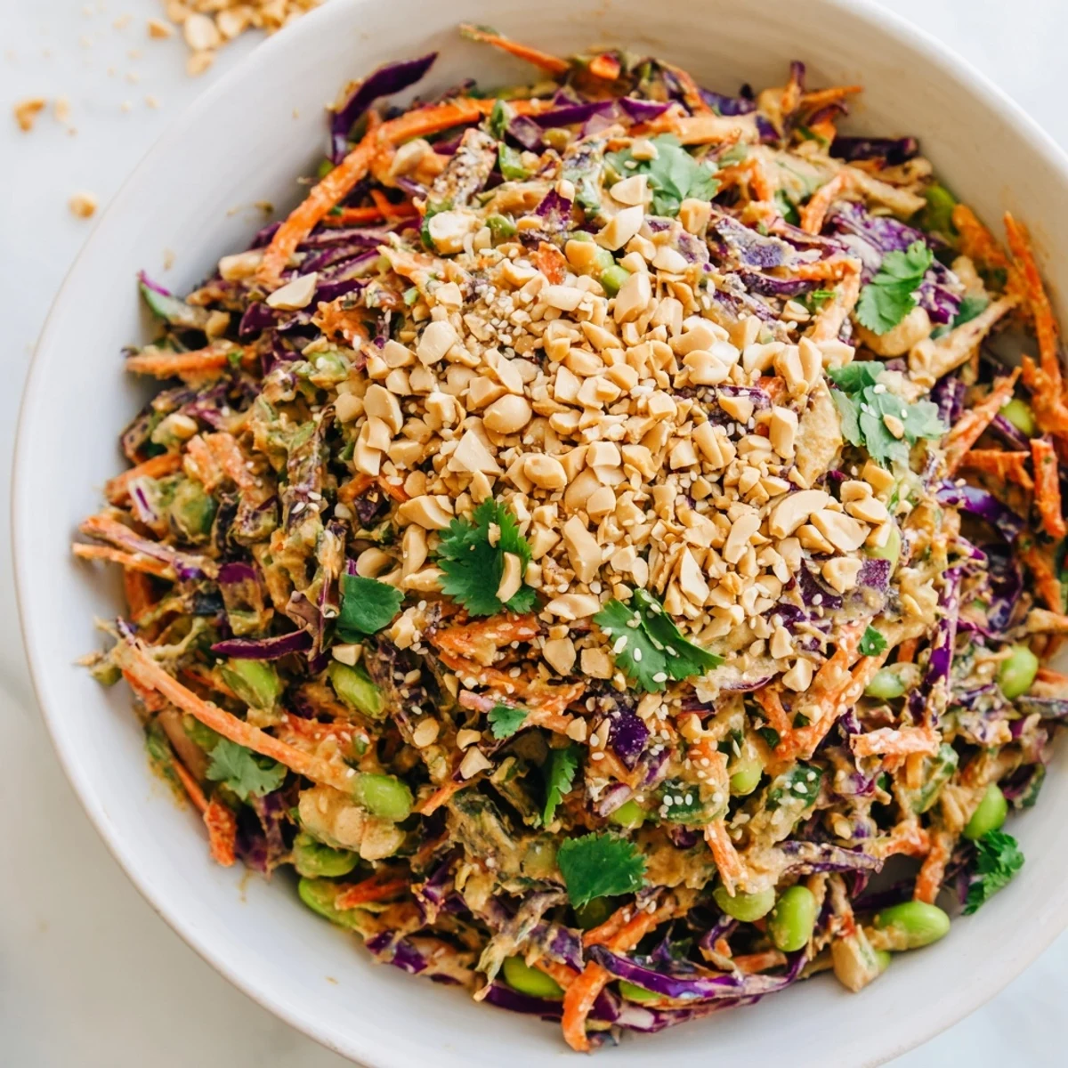 A generous bowl of Crunchy Thai Peanut Salad topped with chopped peanuts and fresh cilantro, served with lime wedges.