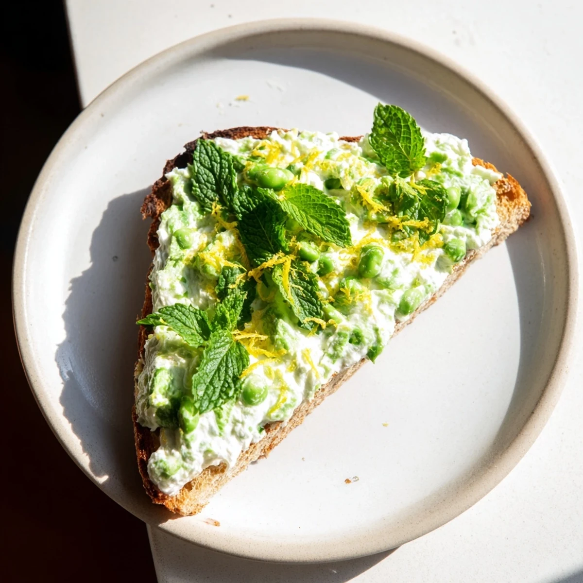 Creamy pea and mint ricotta toast garnished with lemon zest on golden sourdough slices, perfect for a bright, fresh breakfast.  