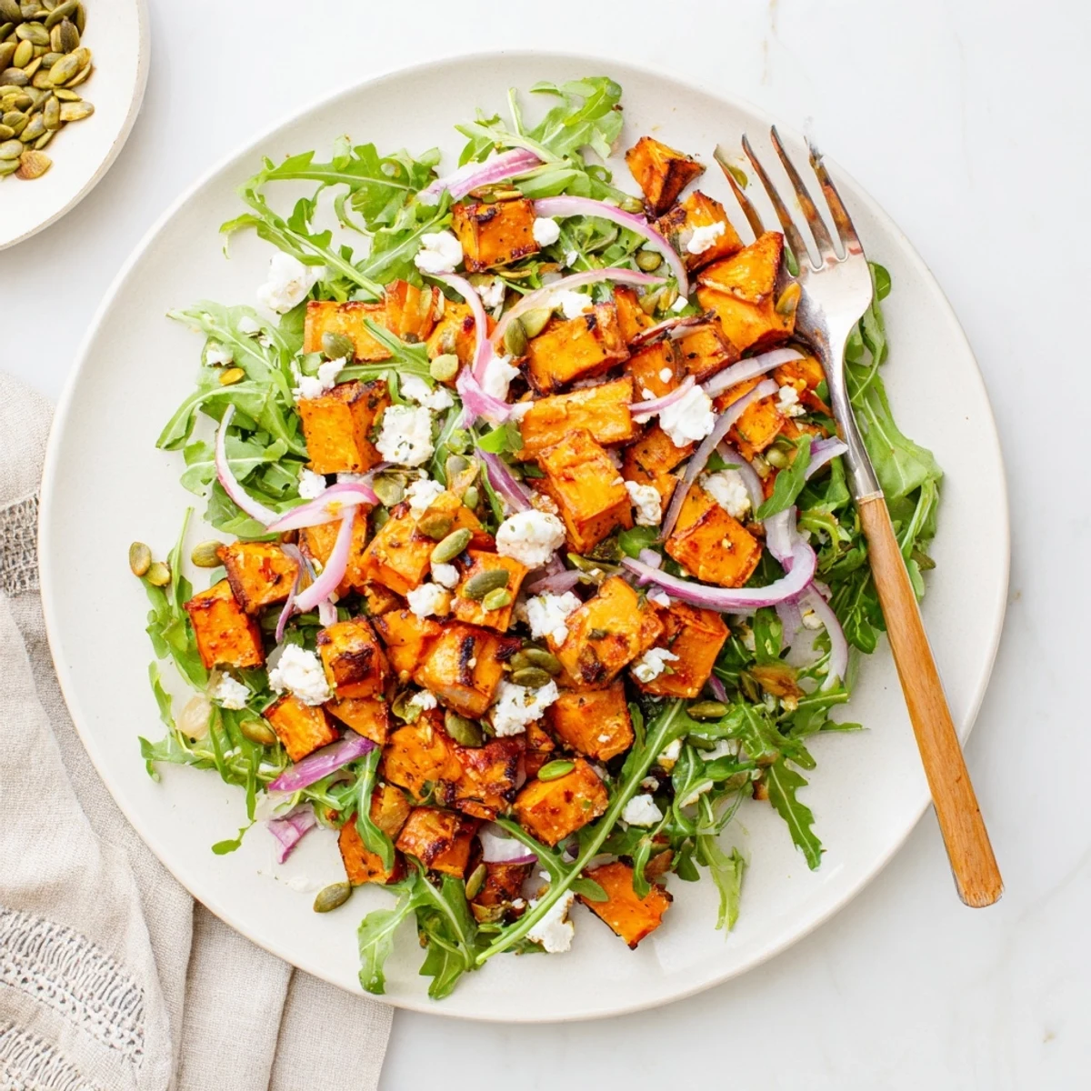 Warm roasted sweet potato salad served over peppery arugula with feta and crunchy seeds.