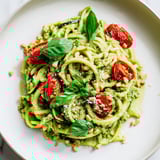 Creamy avocado pesto coats tender zoodles, Italian-inspired dish with fresh basil garnish.