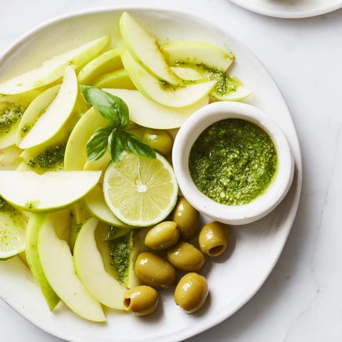 Emerald City snack board, a vibrant appetizer offering green apples, olives, and pesto for dipping.