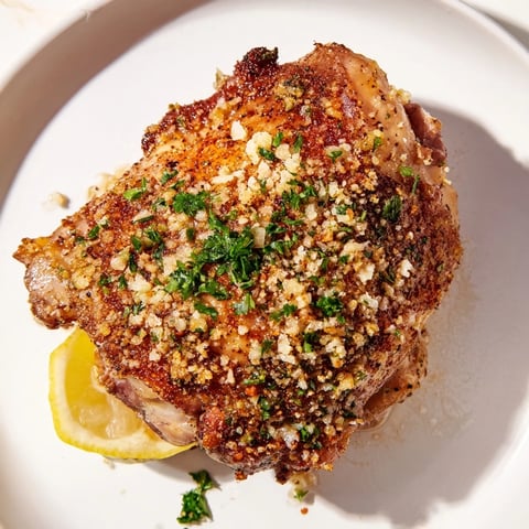 Golden, crispy garlic chicken thighs with flavorful skin, ready to serve with lemon wedges.