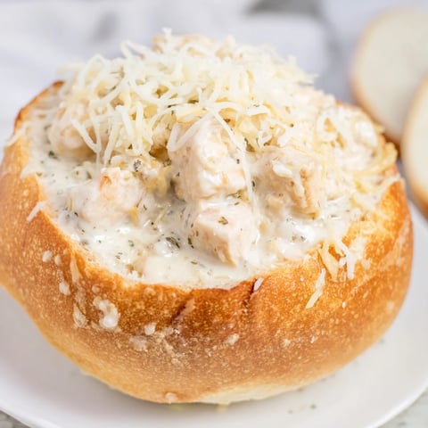 A golden bread bowl filled with creamy Chicken Alfredo, topped with melted Parmesan and fresh parsley.