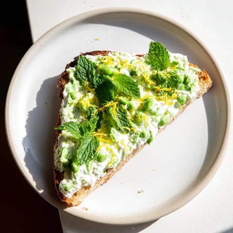 Creamy pea and mint ricotta toast garnished with lemon zest on golden sourdough slices, perfect for a bright, fresh breakfast.  