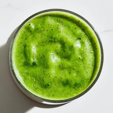 The vibrant green Green Detox Smoothie in a tall glass, topped with a sprinkle of chia seeds and a fresh mint sprig.  