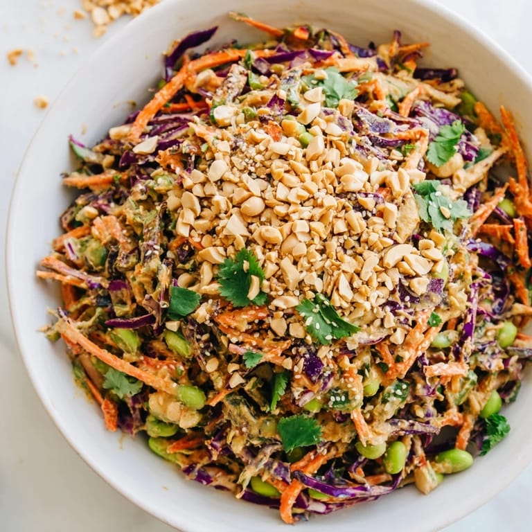 A generous bowl of Crunchy Thai Peanut Salad topped with chopped peanuts and fresh cilantro, served with lime wedges.