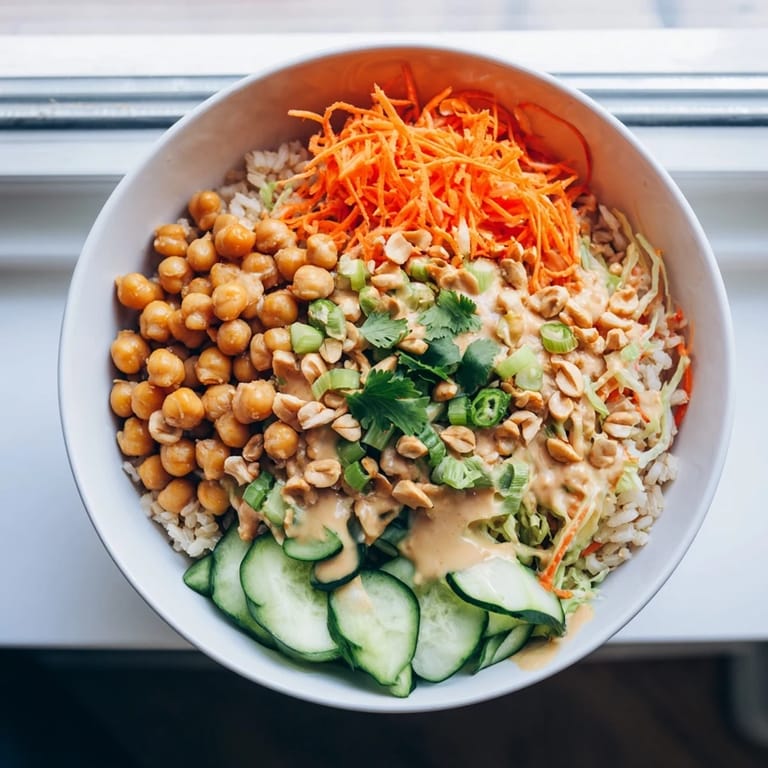 A fresh Peanut Chickpea Rice Bowl featuring tender chickpeas, crisp carrots, cabbage, and cucumber with a drizzle of zesty peanut dressing.