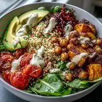 Vibrant quinoa Buddha Bowl topped with caramelized sweet potatoes, crispy chickpeas, and creamy tahini drizzle.