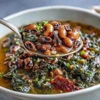 Hearty bowl of soul food black-eyed pea and collard green stew with tender greens and smoky broth. Warm and comforting Southern classic.  